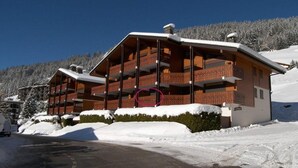 Un chalet in legno a più piani con balconi, circondato da alberi innevati e un cielo sereno.