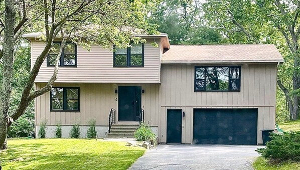 Une maison à deux étages avec un garage à l’avant, une porte d’entrée et un petit jardin devant.