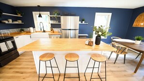 A modern kitchen with a central island, bar stools, a stainless steel refrigerator, and wooden flooring. - 5 STAR Coastal Farmhouse- Dog Friendly- 3BR in Westerly! Minutes to Beach & Town (Westerly)