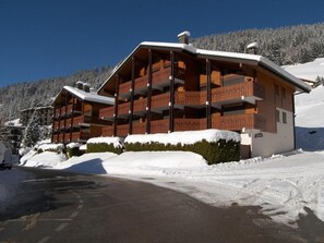A multi-story wooden lodge with balconies, surrounded by snow-covered terrain and a clear sky.