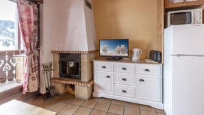 A compact kitchen with a built-in fireplace, a television, and a refrigerator.