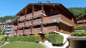 A multi-story wooden building with balconies, surrounded by greenery and a clear sky.