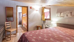 A bedroom with a wooden bed, a chair, a desk, and a mirror. There is a door leading to another room.