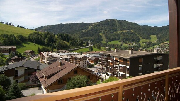 A mountain town with a mix of traditional and modern buildings, a clear view of the surrounding hills, and a balcony overlooking the town.