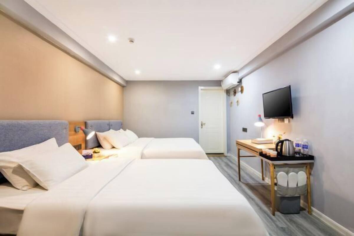 A hotel room with two beds, a desk with a lamp, a television, and a small trash bin.