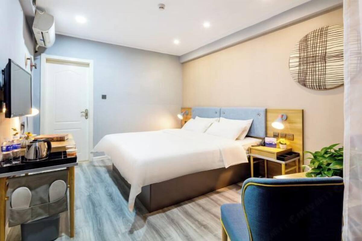 A hotel room with a bed, bedside table, chair, desk, and a TV.