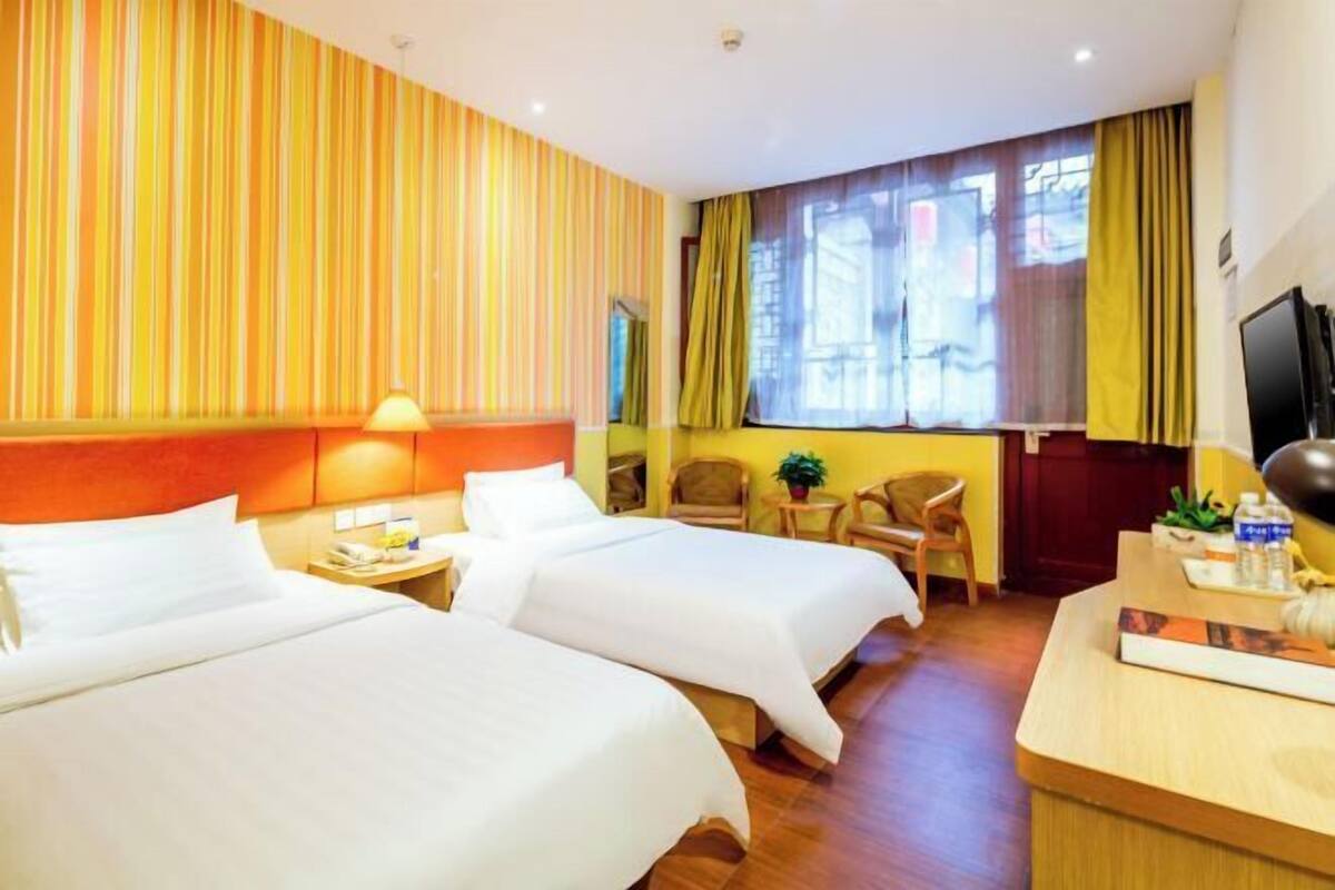 A hotel room with two beds, a desk, a chair, a TV, and a window with curtains.