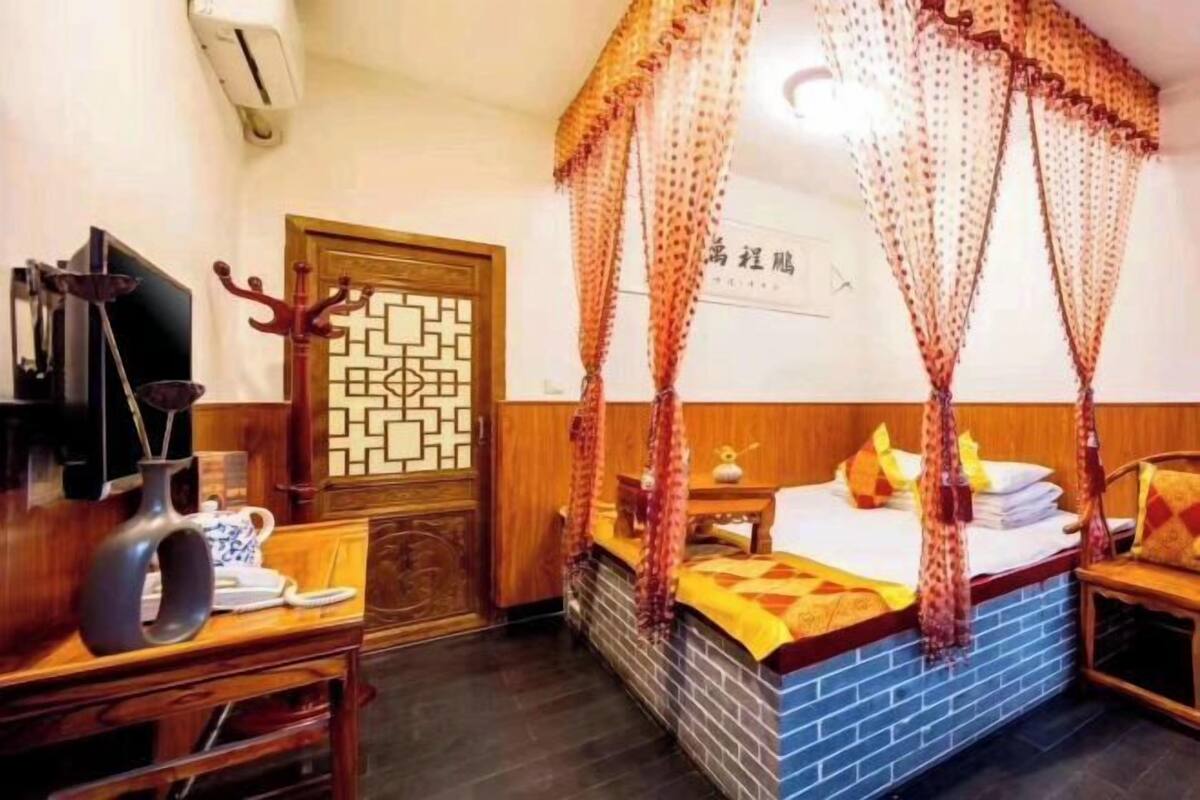 A traditional room with a four-poster bed, a wooden desk, a telephone, and a decorative wall panel.