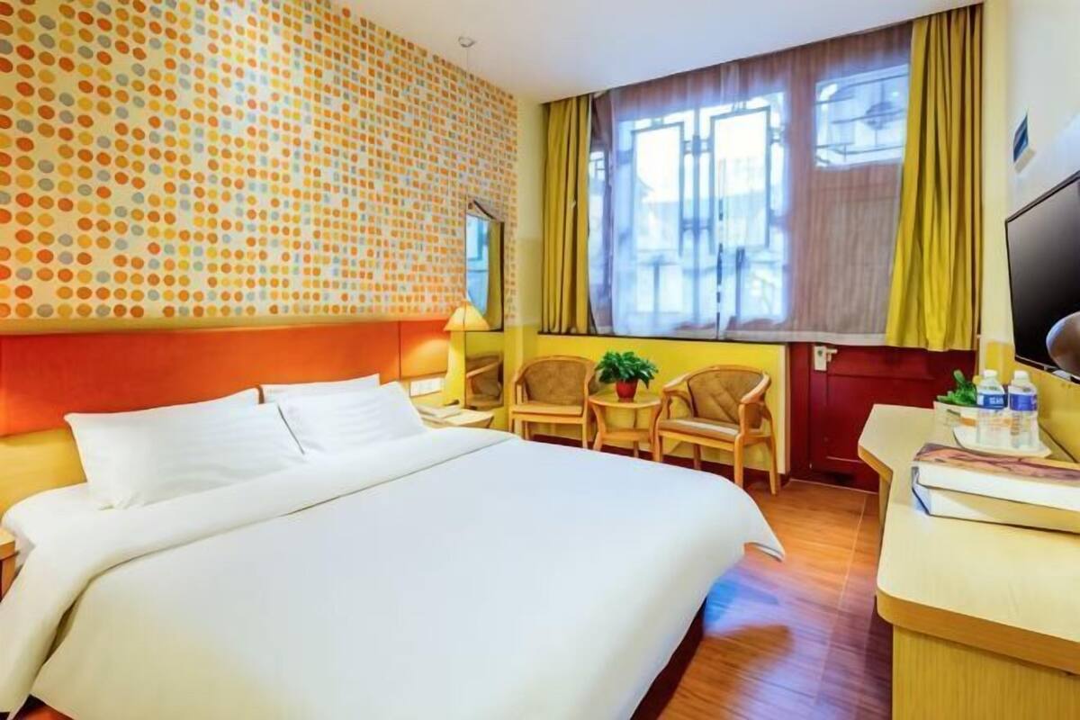 A hotel room with a large bed, a desk, two chairs, a TV, and a window with curtains.