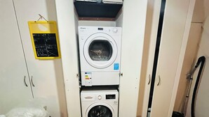 Ein kleiner Waschraum mit zwei übereinander gestapelten Waschmaschinen, einem Wäscheständer und einer Kreidetafel mit Waschanleitungen.
