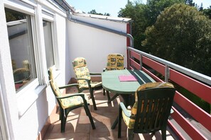 Ein Balkon mit Tisch, vier Stühlen, einem Fenster und einem roten Geländer.