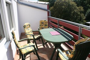Ein Balkon mit zwei Stühlen und einem Tisch, einem roten Geländer und Blick auf Bäume.