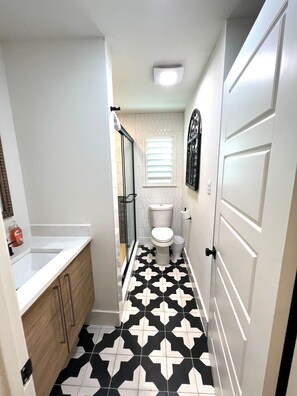 Une petite salle de bain avec un sol carrelé en noir et blanc, des toilettes blanches et un meuble en bois.