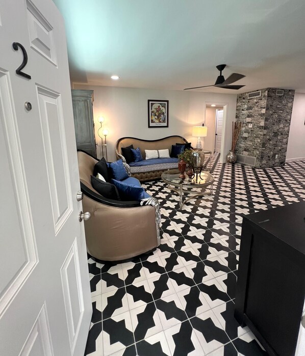 Un salon comprenant un canapé, une table basse et un téléviseur. Le sol est recouvert d’un motif géométrique noir et blanc.