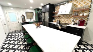 A modern kitchen with a white countertop, green bar stools, a built-in oven, and a patterned backsplash. - Frida Unit #2. Charming 2-bedroom apartment  in delightful Corpus Christi. (Corpus Christi)
