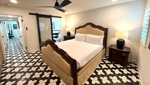 A hotel room with a bed, a nightstand, a lamp, a ceiling fan, and a bathroom visible through an open door. - Frida Unit #2. Charming 2-bedroom apartment  in delightful Corpus Christi. (Corpus Christi)
