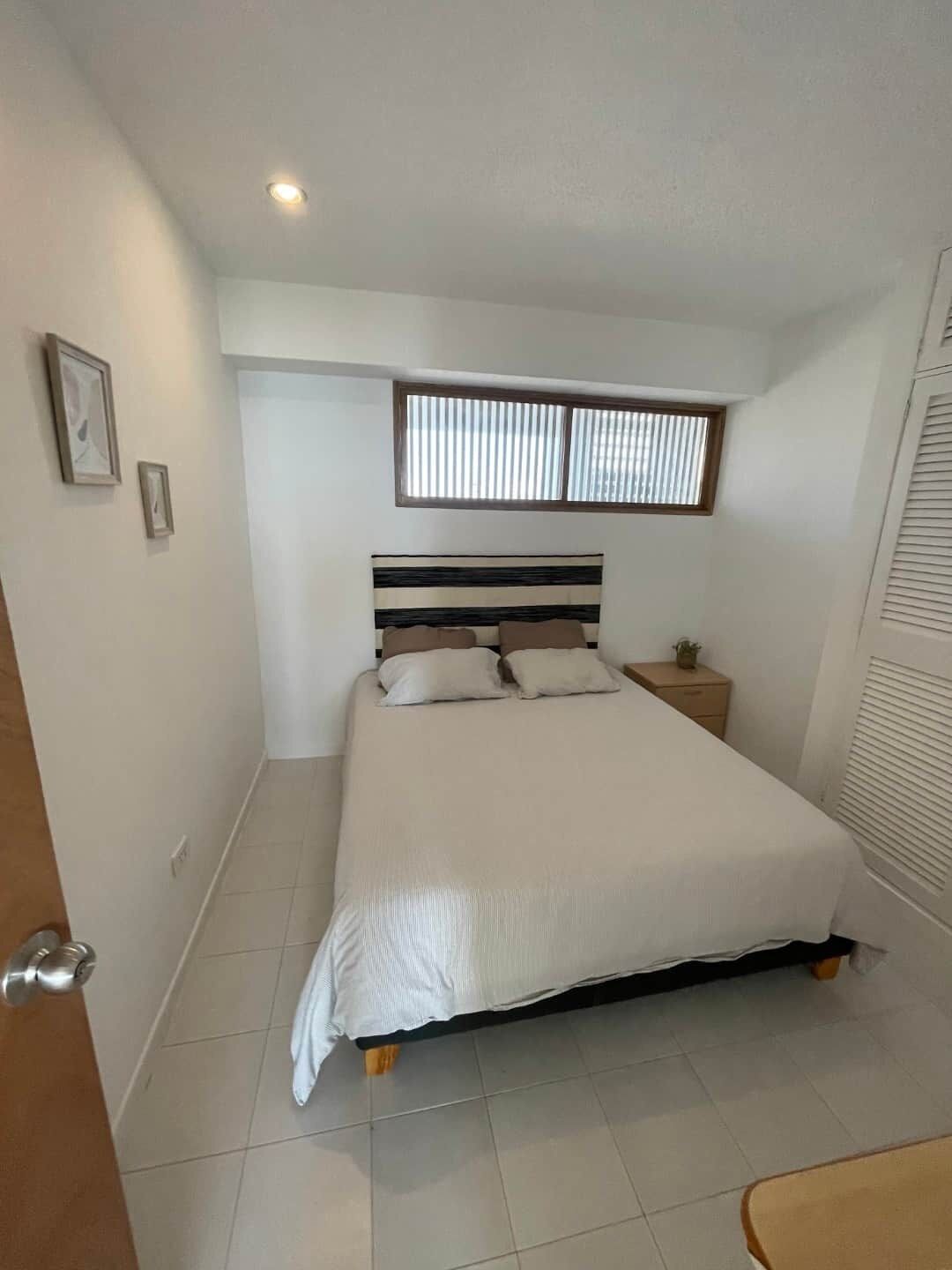 Une chambre à coucher avec un lit, une table de chevet, une fenêtre avec des stores et une porte.