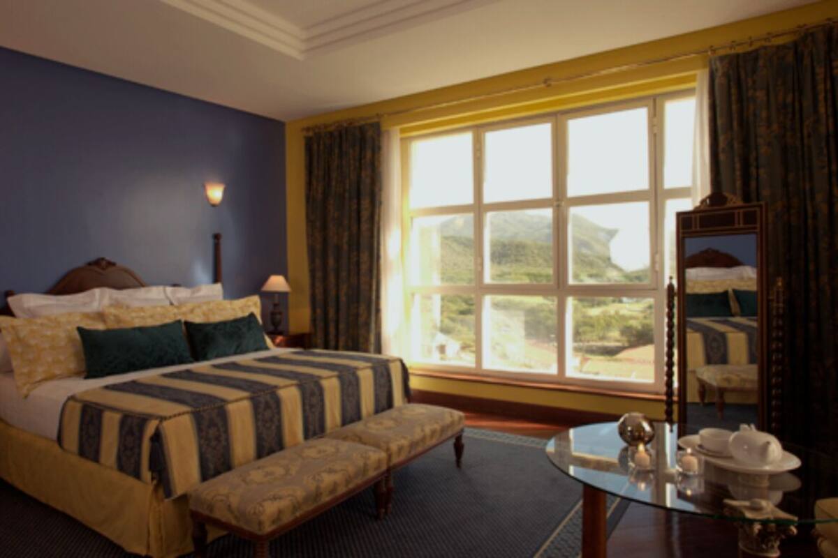 Ein Hotelzimmer mit einem großen Bett, einer Bank, einem kleinen Tisch mit Tee-Service und Blick ins Freie.