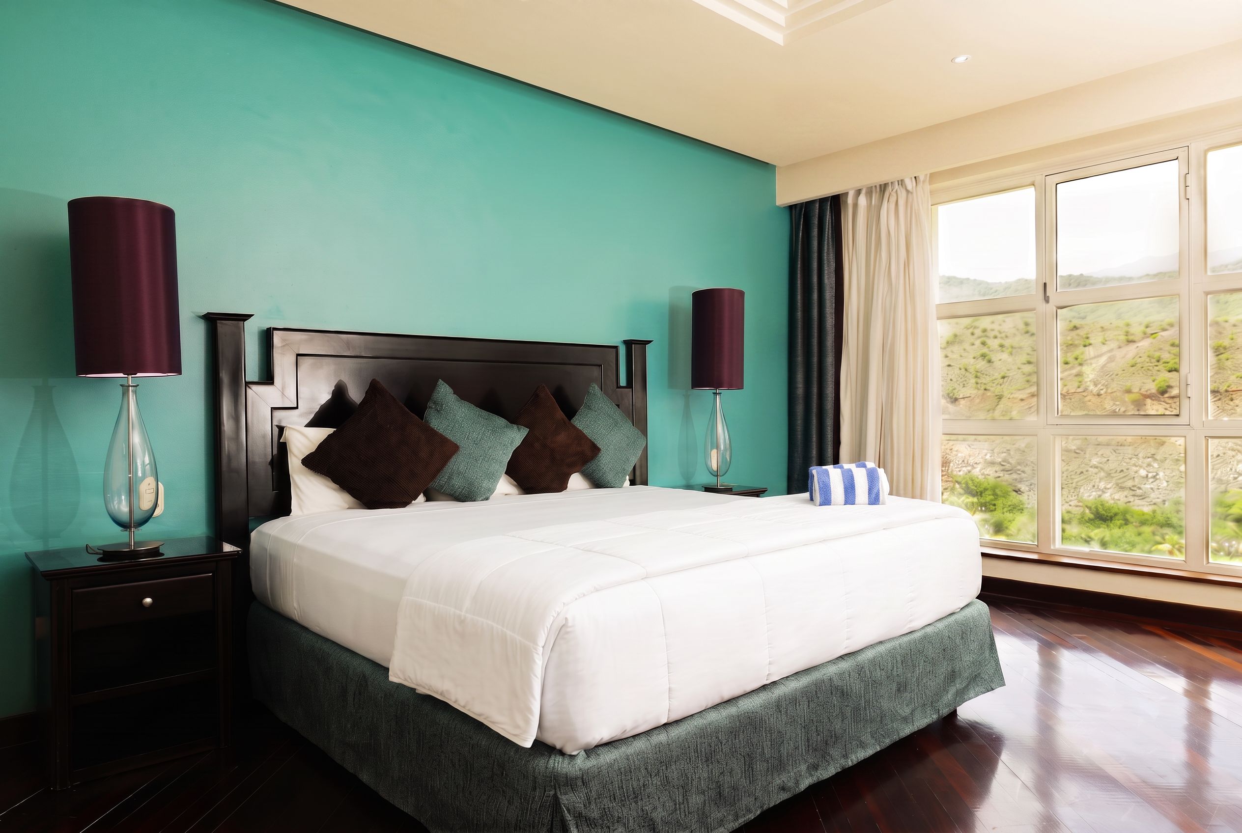 A bedroom with a bed, nightstands, a lamp, a window with a view, and a curtain.