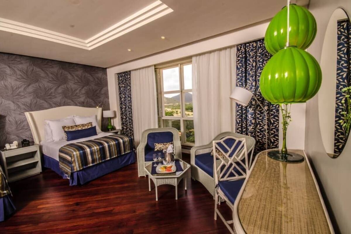 Ein Hotelzimmer mit einem Bett, zwei Sesseln, einem kleinen Tisch mit Tablett, einer Lampe und Blick ins Freie.