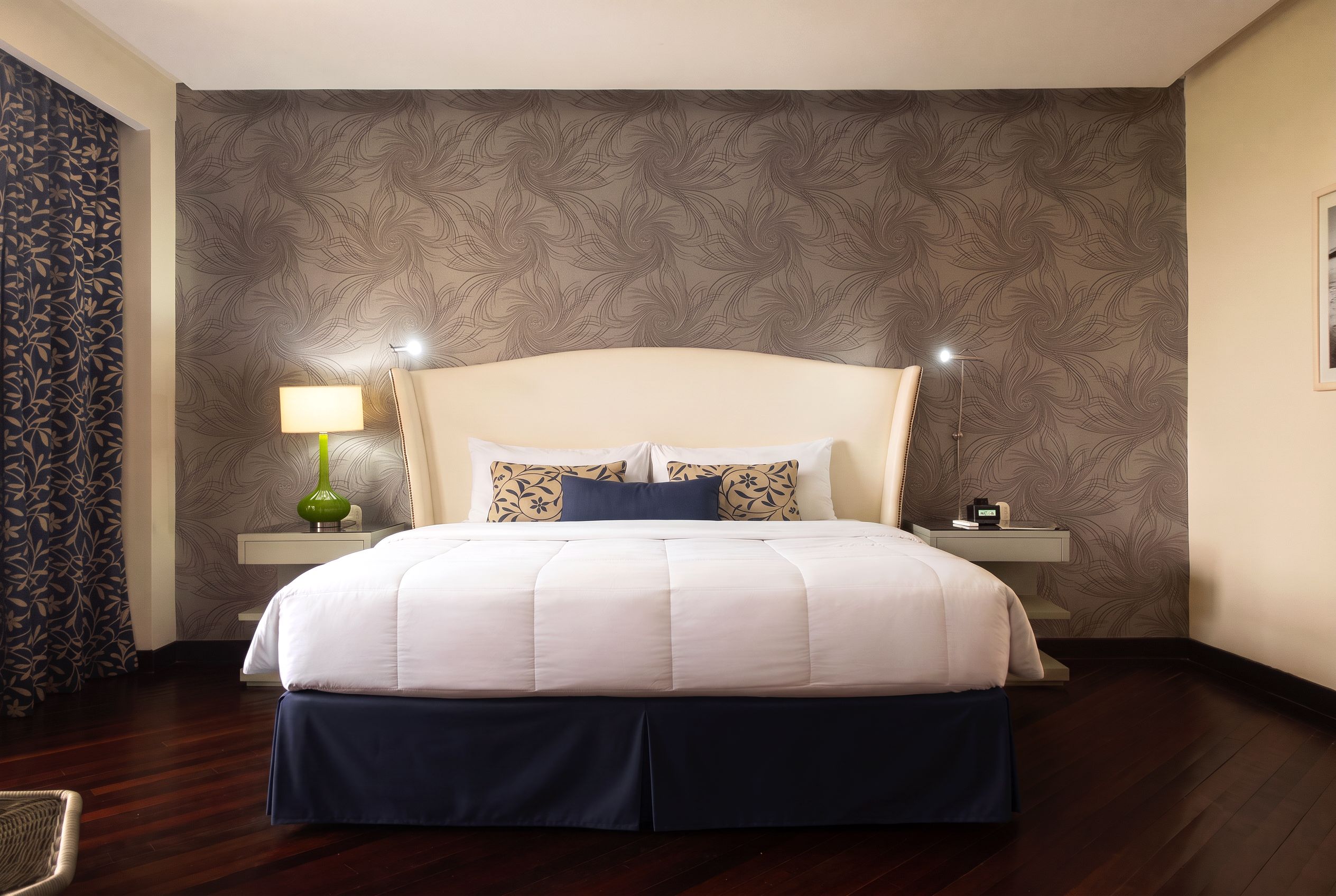 A hotel room with a large bed, two bedside tables, a lamp, and a wall with a swirling pattern.