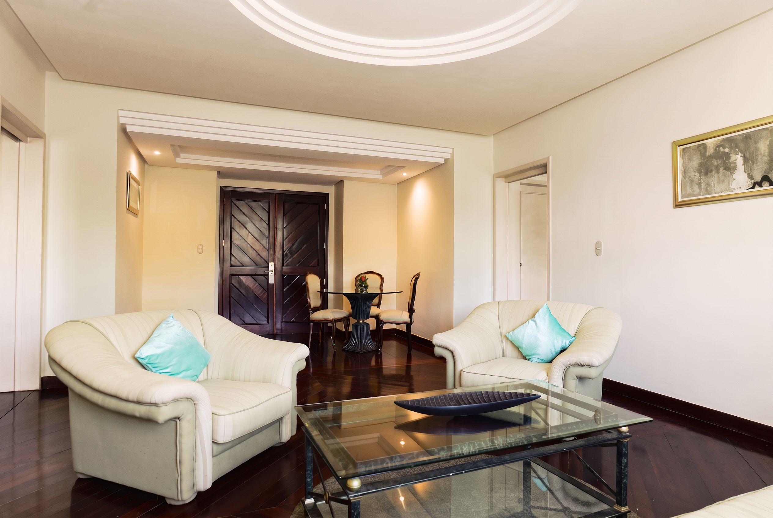 A modern living room with two armchairs, a glass coffee table, and a dining area with a table and chairs.