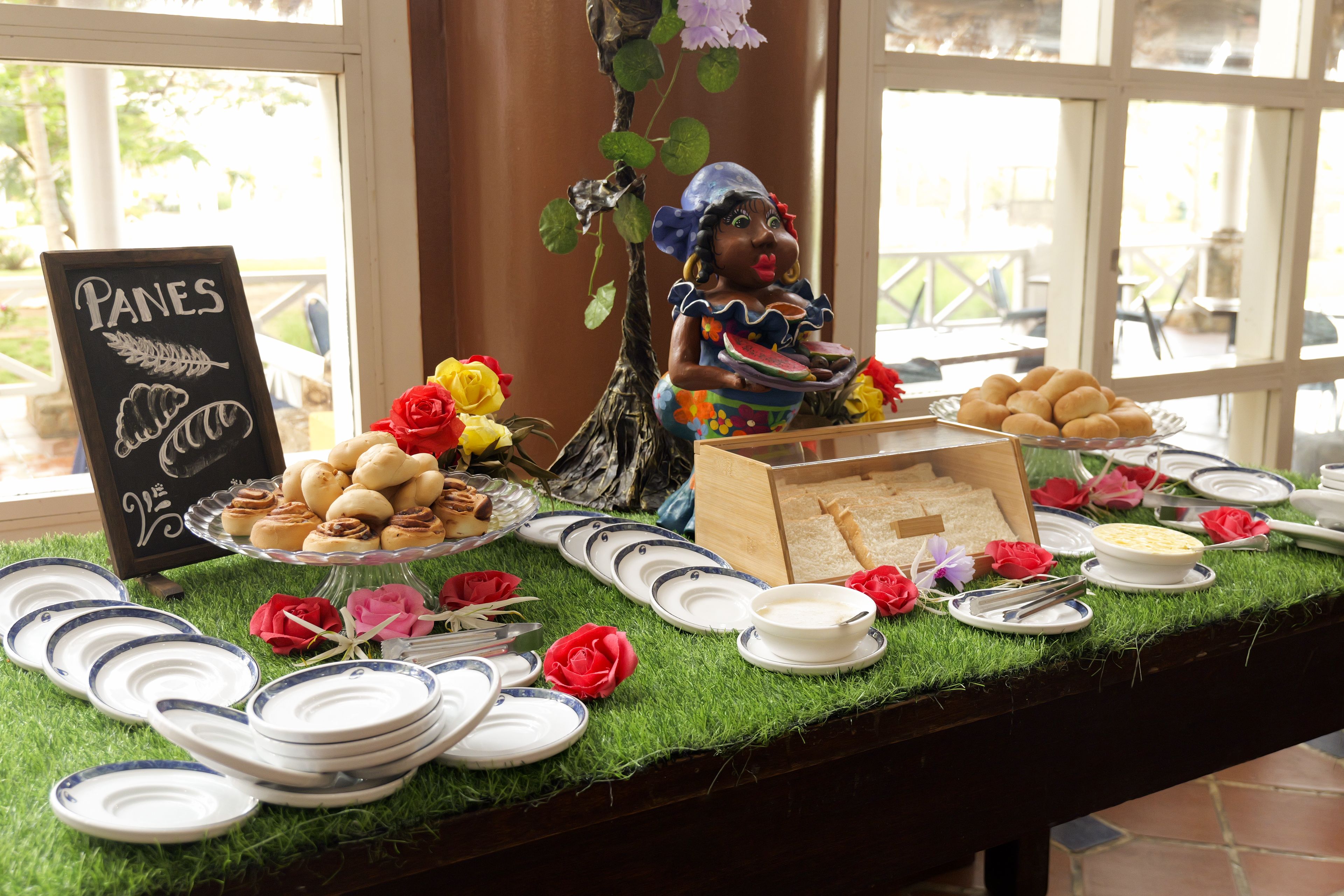 Une table de buffet avec divers plats, assiettes et un panneau indiquant « PANES ».