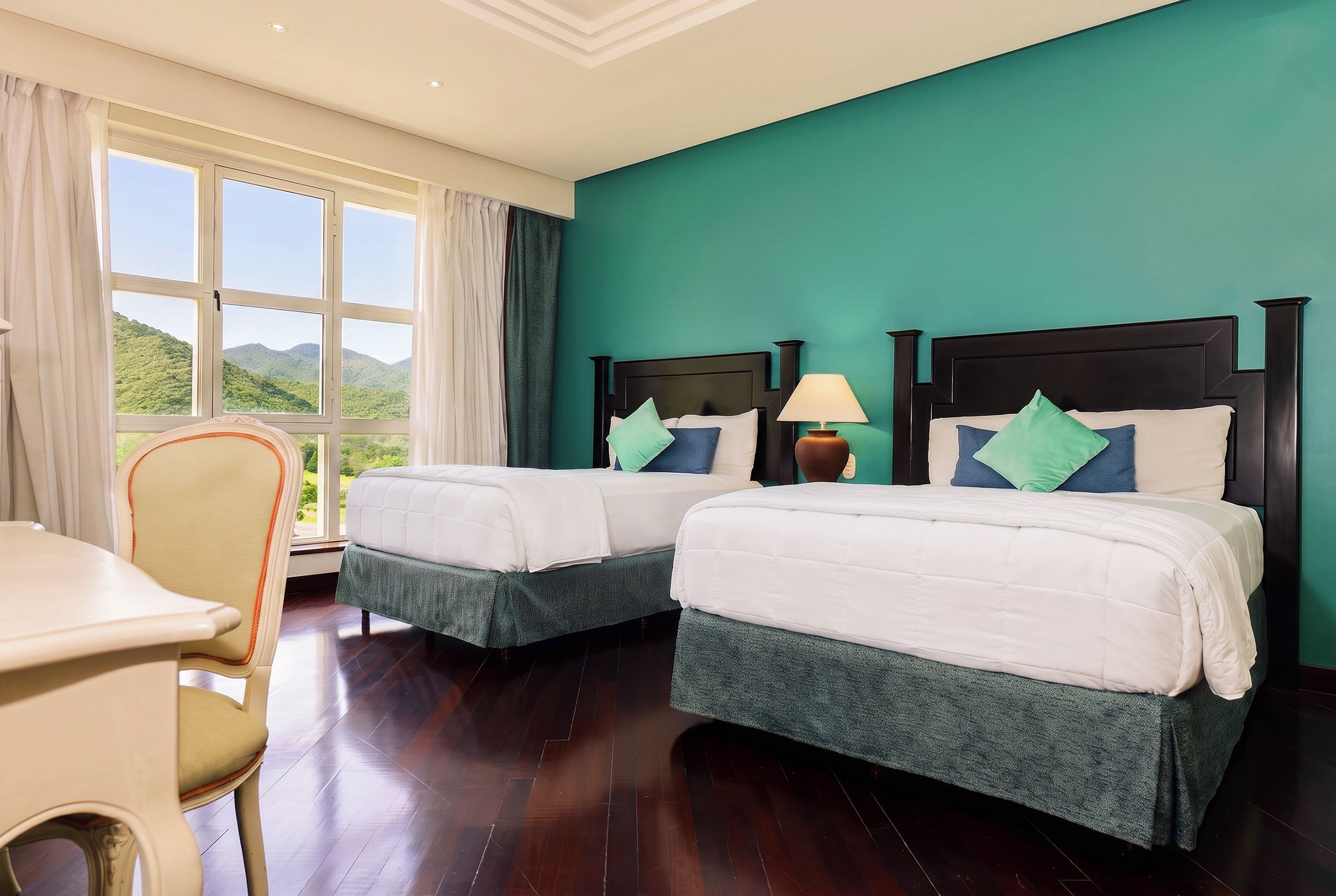 A hotel room with two beds, a desk, and a view of the outdoors.