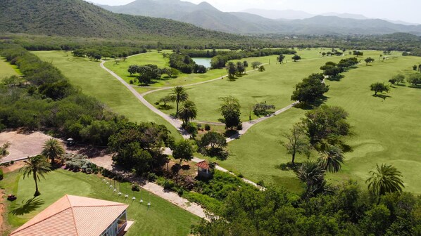 Vista aérea de un campo de golf con un lago, rodeado de vegetación exuberante y montañas al fondo.