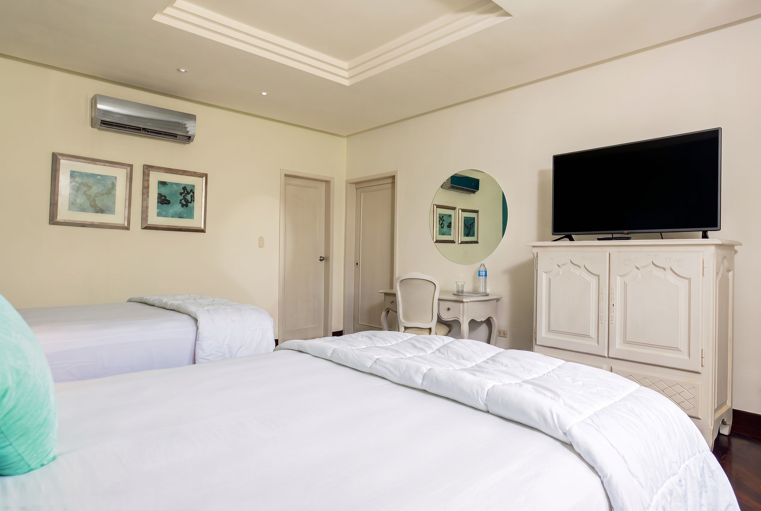 A hotel room with two beds, a television, a desk with a chair, and a mirror.