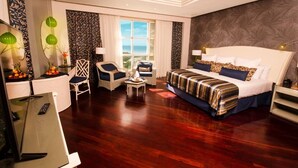 A hotel room with a large bed, a desk with a computer, a chair, a small table with fruit, and a view of the sea through the window. - Hesperia Isla Margarita Todo Incluido (Matasiete)