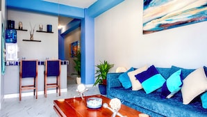 A modern living room with a blue sofa, wooden coffee table, and a kitchen area with bar stools. - Romantic Zone newly renovated, super comfortable, one bedroom view condo (Puerto Vallarta)