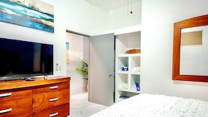 A bedroom with a bed, a TV on a wooden dresser, a wardrobe, and a shelf with towels. - Romantic Zone newly renovated, super comfortable, one bedroom view condo (Puerto Vallarta)