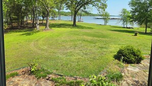 A grassy area with trees and a body of water in the background. - Lakehouse on Ky Lake-Lakefront, Park like backyard, Covered Dock, Firepit. (Benton)