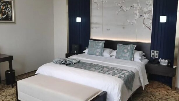 Ein Hotelzimmer mit Bett, Nachttischen, einem Schreibtisch und einer dekorativen Wandverkleidung.