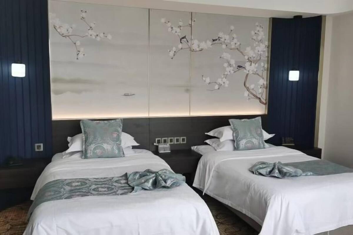 Una camera d'albergo con due letti, un grande murale e un comodino con una lampada.