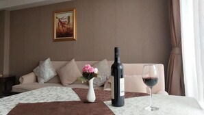 Ein Hotelzimmer mit einer Couch, einer Vase mit Blumen, einer Weinflasche und einem Weinglas auf einem Tisch.