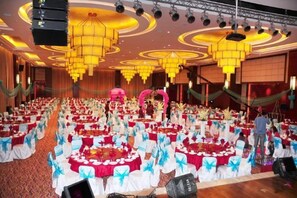 Une salle de banquet avec des tables rondes, une scène et un lustre.