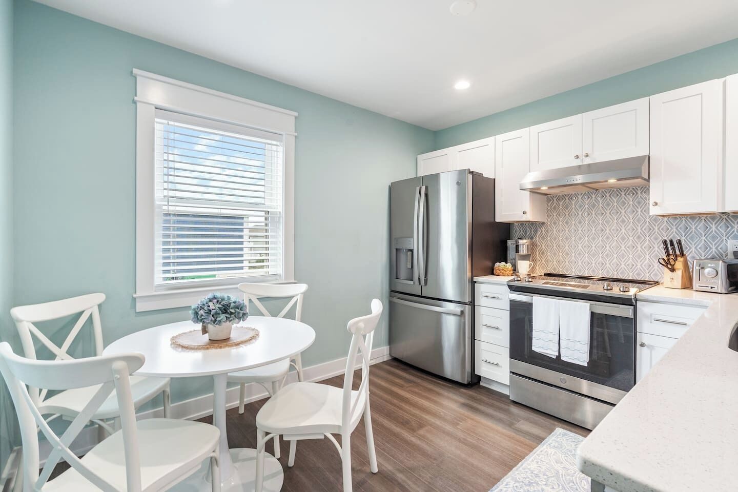 A modern kitchen with white cabinets, stainless steel appliances, and a dining area with white chairs and a round table.