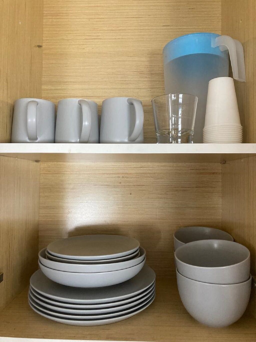 Une étagère en bois sur laquelle sont empilées des assiettes, des bols et un pichet bleu.