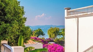 A view of a coastal area with lush greenery and purple flowers, a white building with a balcony, and a clear sky. - Dali Canger Yilong Hotel (Dali City)