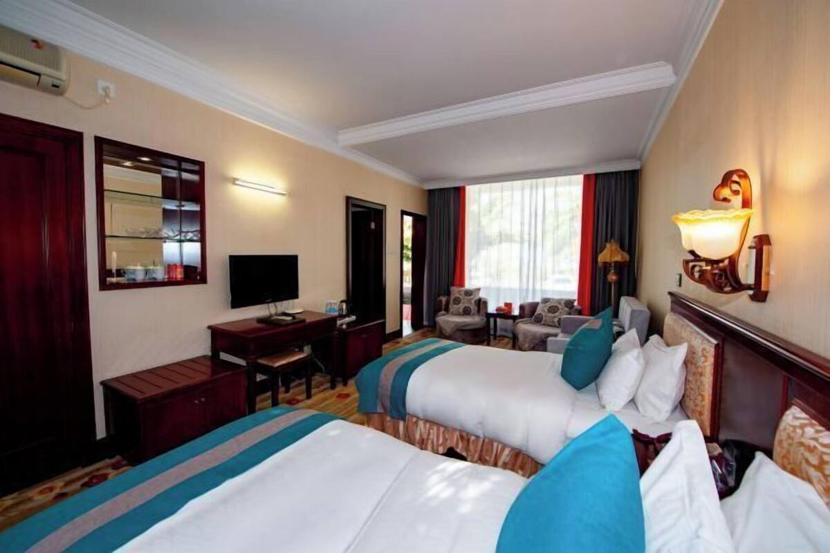 A hotel room with two beds, a desk, a television, and a window with curtains.