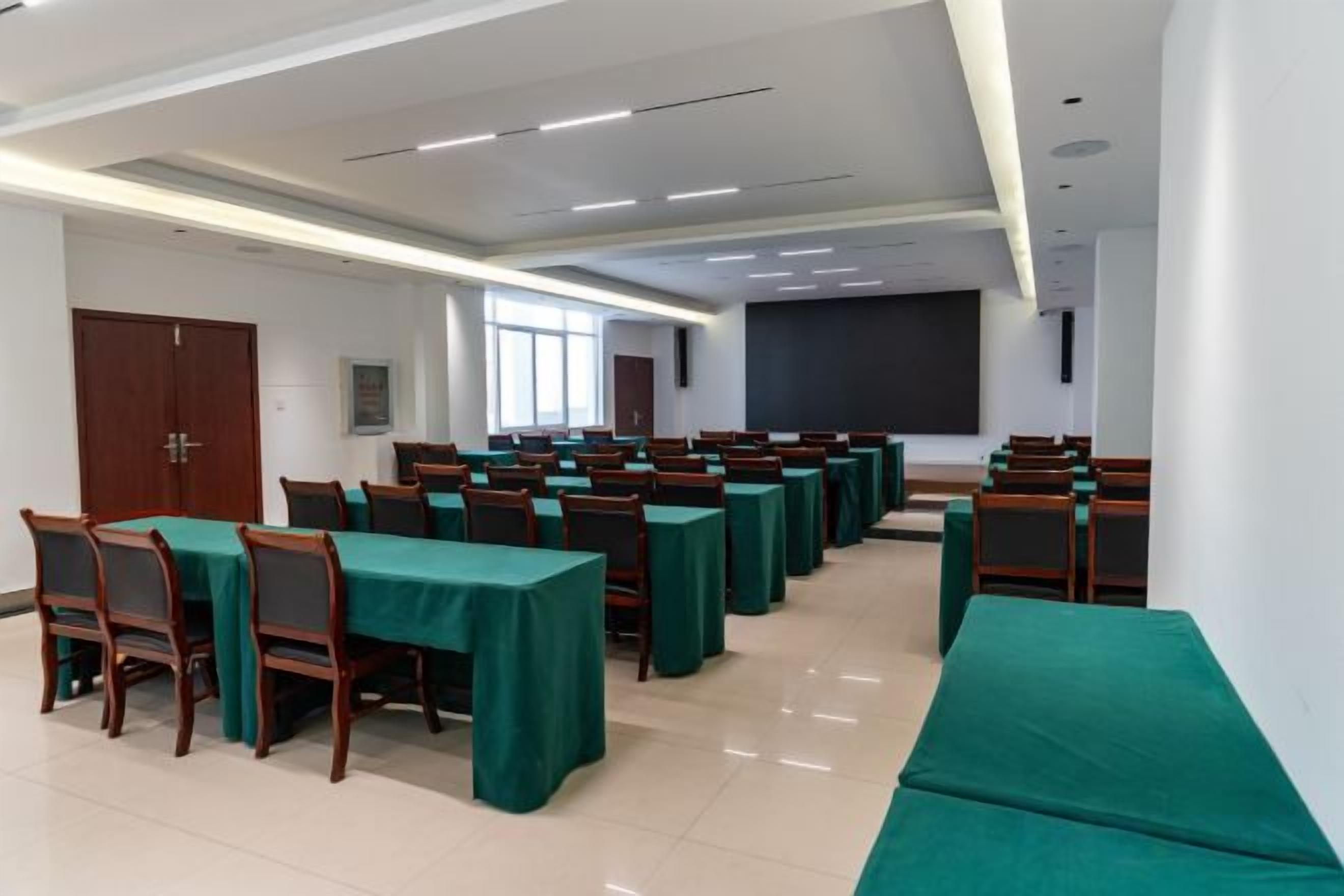 A conference room with rows of tables and chairs, a projector screen, and a large window.