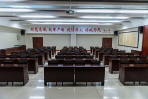 A lecture hall with rows of wooden desks and chairs, a projector screen, and a banner with Chinese characters.