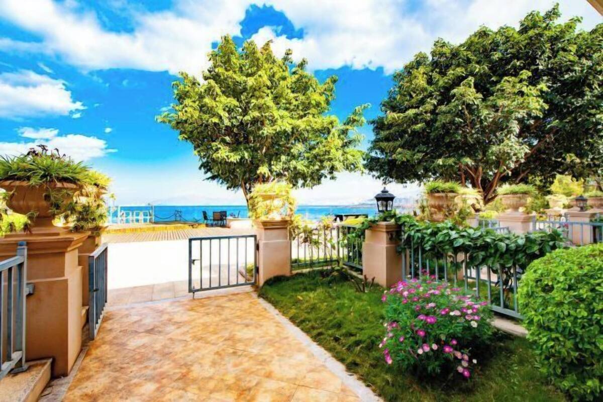 A garden with a view of the sea, a tiled patio, and a metal fence.