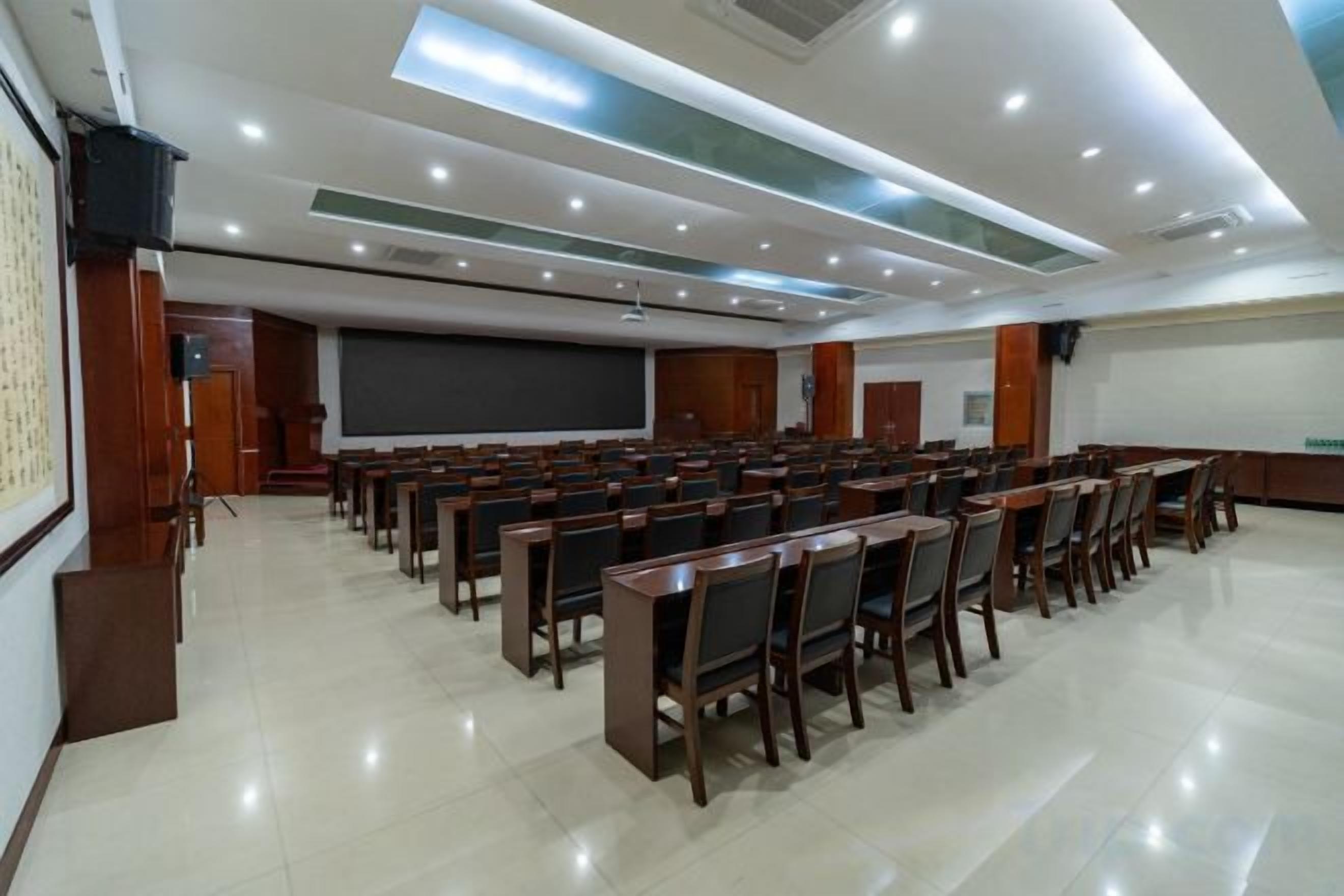 Uma sala de conferência com fileiras de cadeiras, uma tela de projetor e um espaço para apresentações.