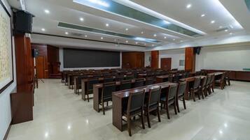 Uma sala de conferência com fileiras de cadeiras, uma tela de projetor e um espaço para apresentações.
