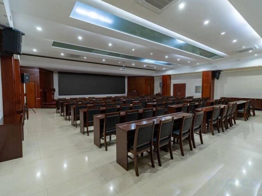 Uma sala de conferência com fileiras de cadeiras, uma tela de projetor e um espaço para apresentações.