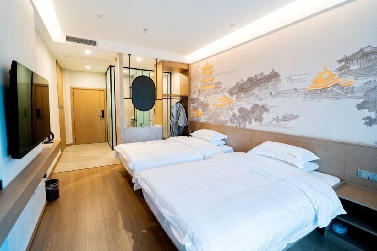 A hotel room with two beds, a TV, a wall with artwork, and a wooden floor.