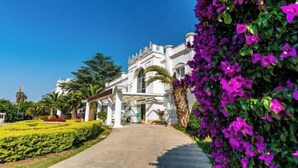 A white building with a covered entrance, surrounded by well-maintained gardens and a clear sky. - Dali Canger Yilong Hotel (Dali City)